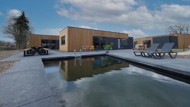 En moderne bygning med swimmingpool, udendørs siddepladser og træfacade.