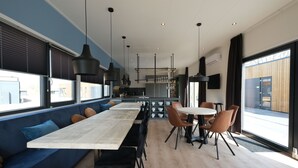 Et moderne spiseområde med et langt træbord, sorte stole og en blå polstret bænk.