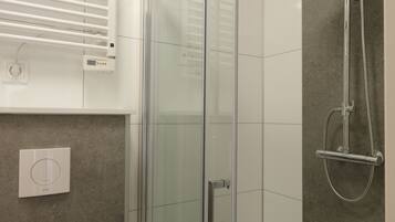 A modern bathroom with a glass shower enclosure, a handheld showerhead, and a toilet.
