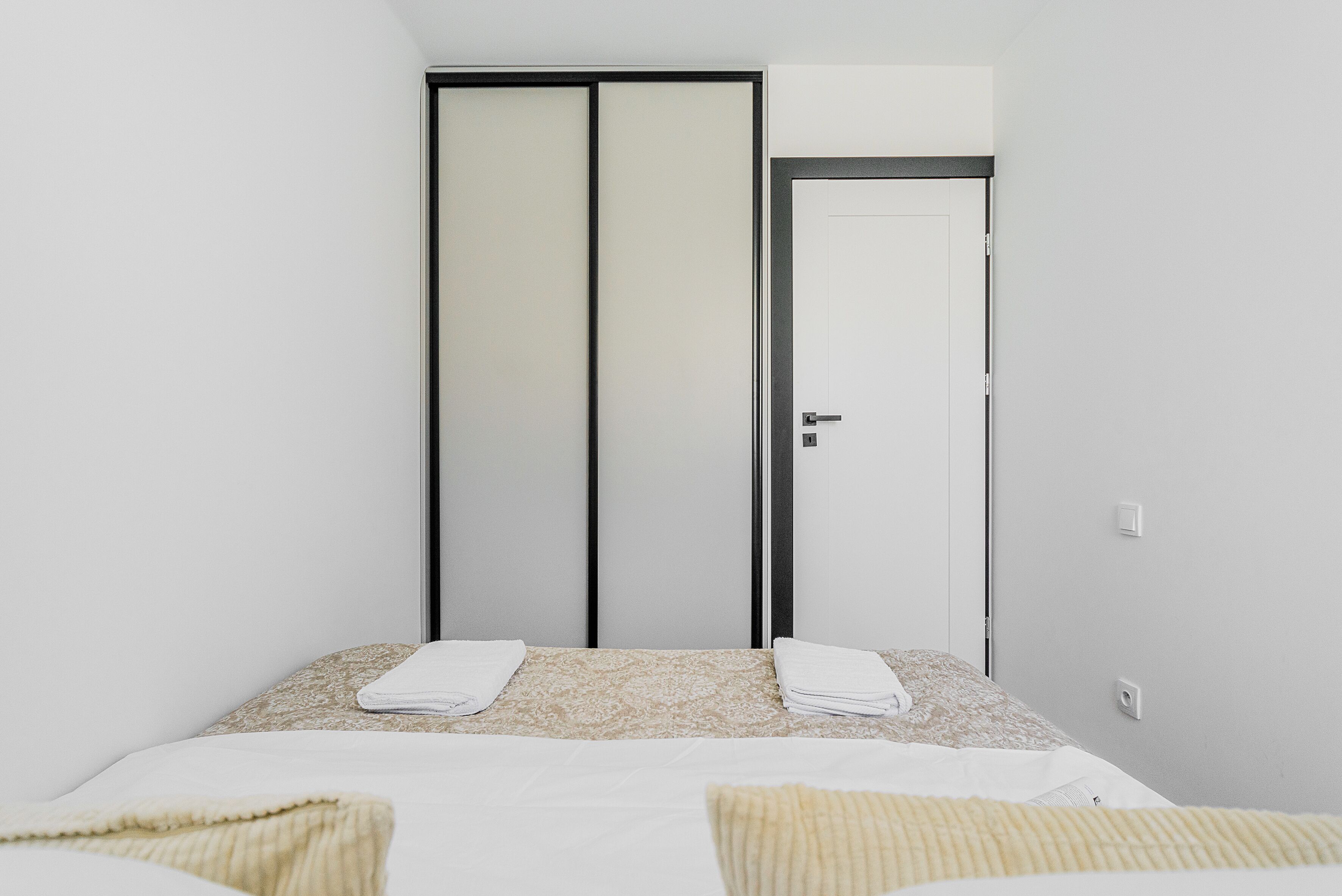 A bedroom with a bed, two towels, a door, and a light switch.