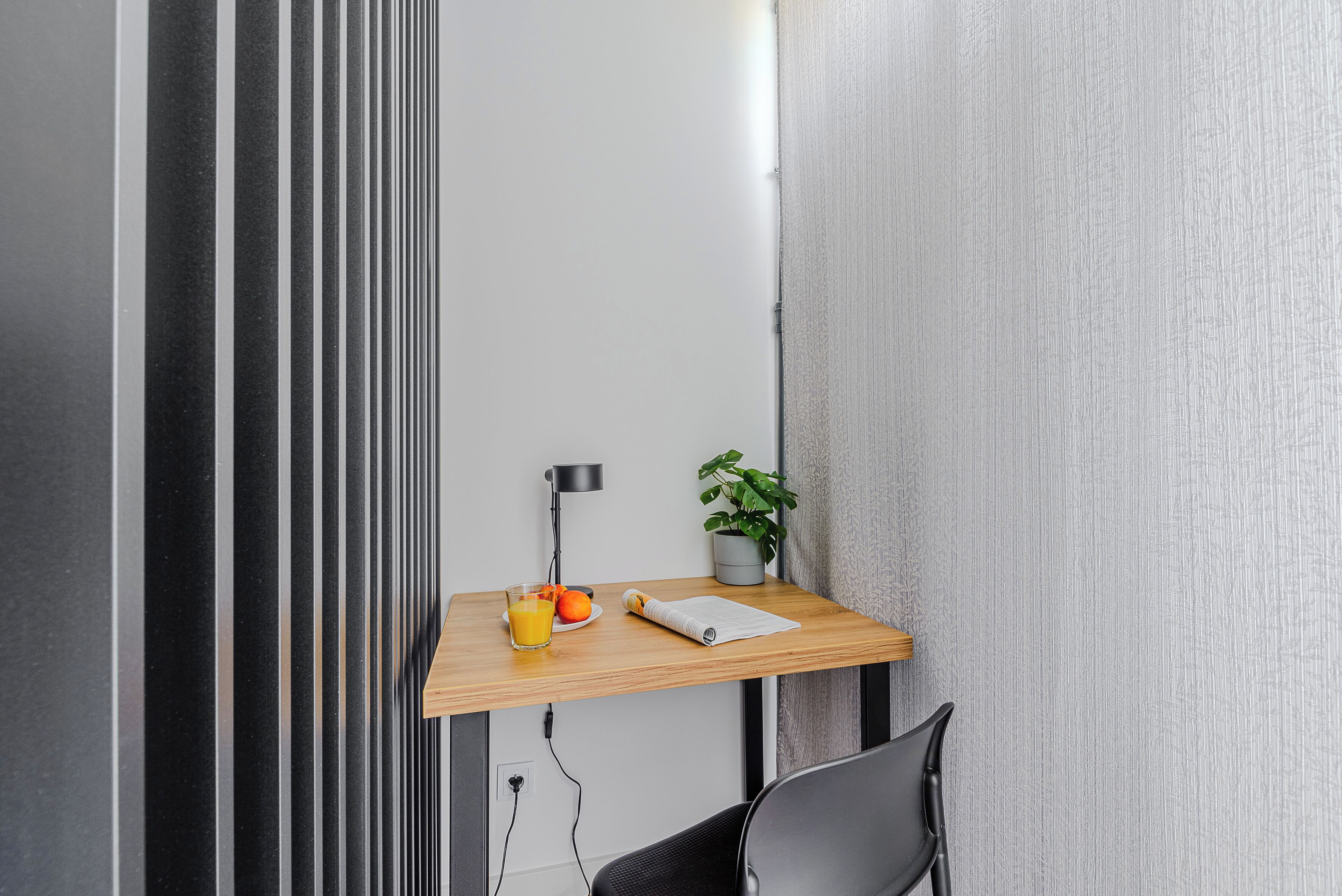 A small workspace with a wooden desk, a black chair, a potted plant, a glass of orange juice, and a notebook.