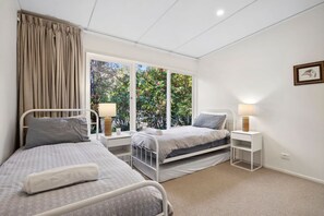 Een slaapkamer met twee bedden, een raam met gordijnen, bedlampjes en een klein nachtkastje.