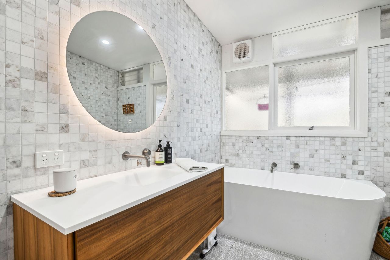 Un baño moderno con una bañera independiente, un espejo grande y un tocador blanco con un gabinete de madera.