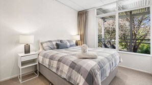 A bedroom with a bed, bedside tables, a window with curtains, and a view of trees. - Nella (Lorne)
