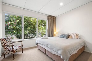 A bedroom with a bed, a chair, a window with curtains, and a view of greenery outside.