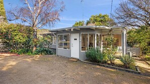 A single-story house with a covered porch, a front door, and a small garden area with various plants. - Nella (Lorne)