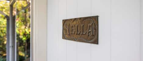 Ein Metallschild mit dem Schriftzug 'NELLAS', an einer weißen Wand angebracht.
