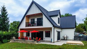 Ein modernes, zweistöckiges Haus mit Balkon, einer Terrasse mit roten Stühlen und Sonnenschirmen sowie einem Grillbereich.