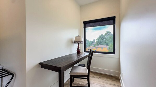 A small dining area with a dark wooden table, a single chair, and a table lamp. A window with a view of a house and trees is visible. - the Signal, New Cedar Sauna! (Zurich)
