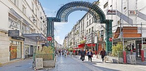 Une rue bordée d’une arche métallique, de boutiques et d’où l’on peut voir des piétons.