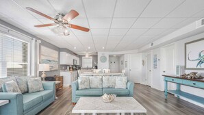 A spacious living room with a ceiling fan, a kitchen in the background, and a dining area.