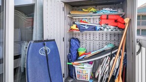 A small outdoor storage area with a blue mat, two buckets, a paddle, and various items stored on shelves.