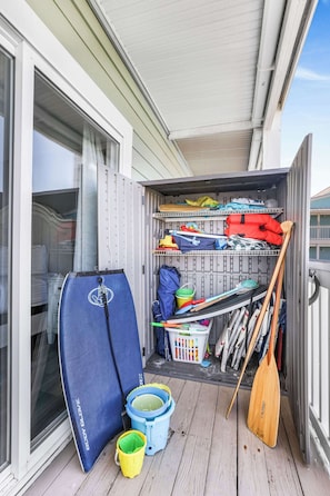 Un petit espace de rangement extérieur avec un tapis bleu, deux seaux, une pagaie et divers objets rangés sur des étagères.