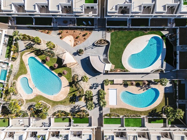 Vue aérienne d’un hôtel moderne doté de plusieurs piscines, d’espaces paysagers aménagés et d’une cour intérieure.