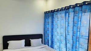 A bed with white bedding, a dark headboard, and a blue curtain with a tree pattern. - Parinay Vatika Banquet & Party Lawn (Haldwani)