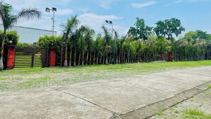 A concrete pathway leading to a gated entrance with a row of palm trees and a building in the background. - Parinay Vatika Banquet & Party Lawn (Haldwani)
