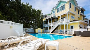 A pool area with lounge chairs and a two-story building with a balcony. - Golf Cart Friendly, Pool, Game Room & Resort Perks (Corolla)