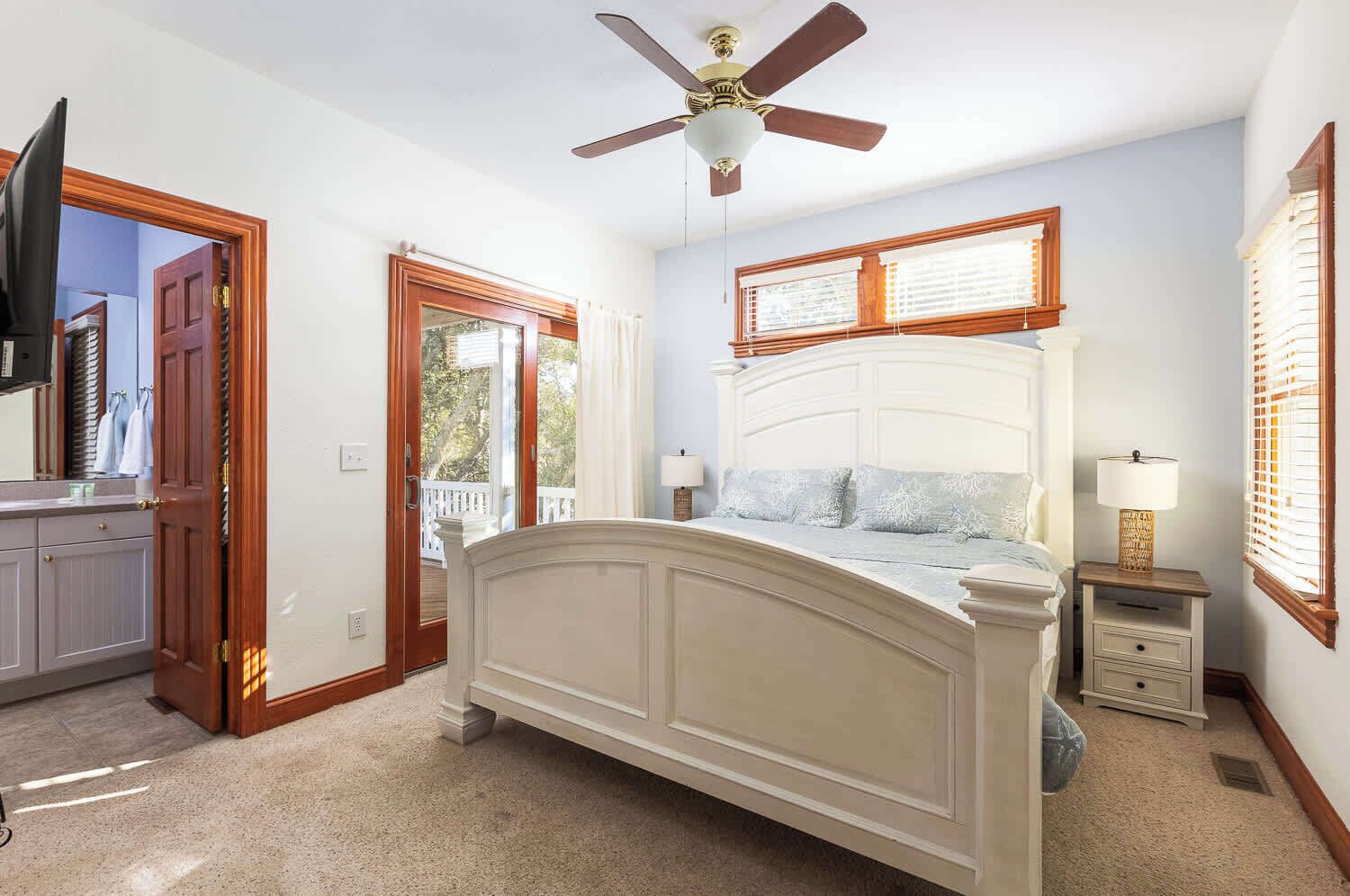 A bedroom with a bed, a ceiling fan, a nightstand with a lamp, and a window with blinds.