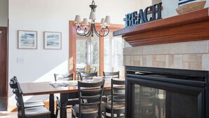 A dining area with a wooden table, chairs, a chandelier, and a fireplace. - Golf Cart Friendly, Pool, Game Room & Resort Perks (Corolla)