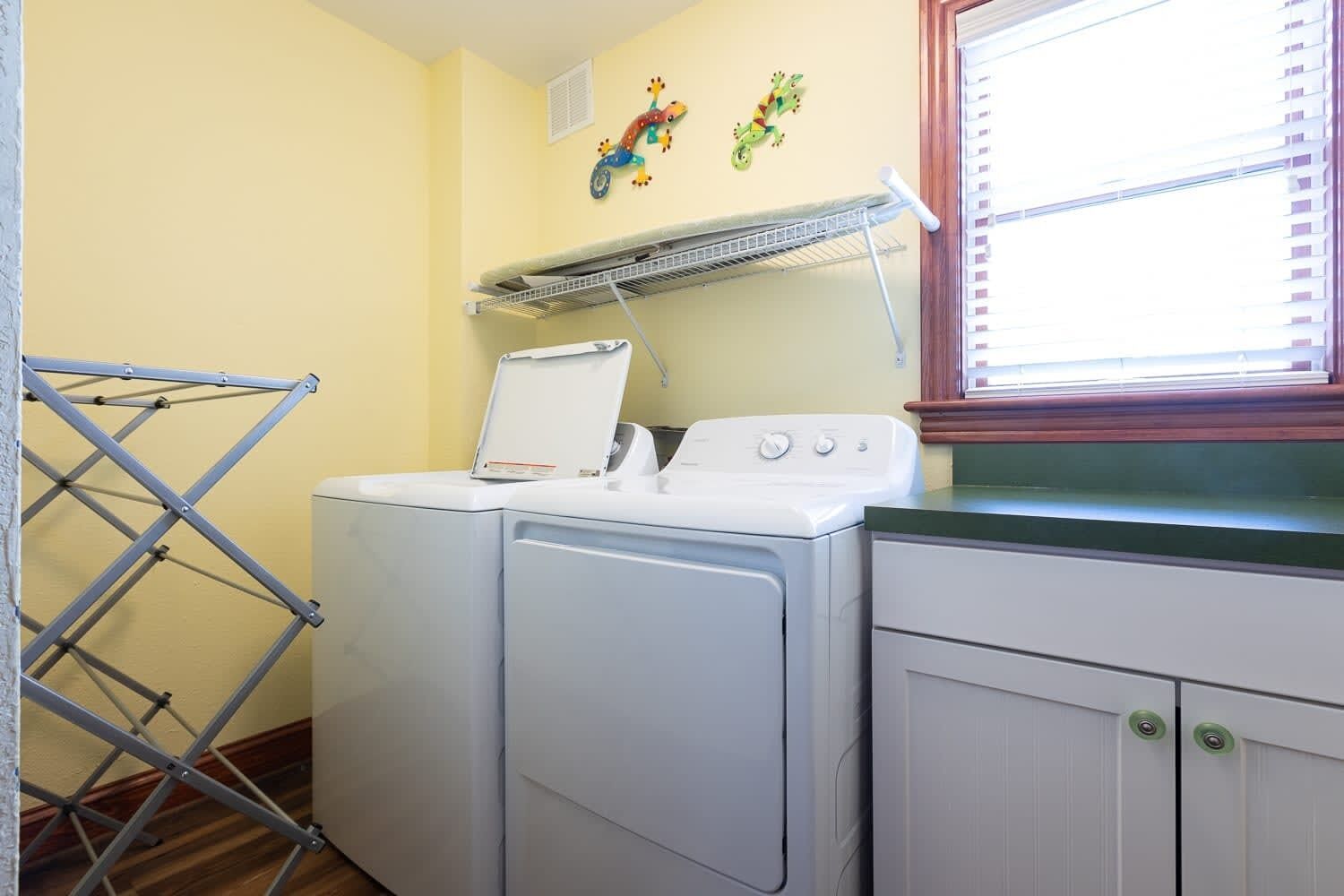 A laundry area with a washing machine and dryer, a drying rack, and a window with blinds.
