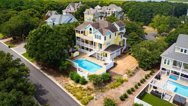 A large, multi-story house with a swimming pool, surrounded by lush greenery and a view of the water. - Golf Cart Friendly, Pool, Game Room & Resort Perks (Corolla)