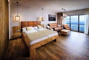 A spacious bedroom with a large bed, a wooden headboard, a wooden bench, and a view of the mountains through large windows. - APLEND Monte Móry (Štrba)