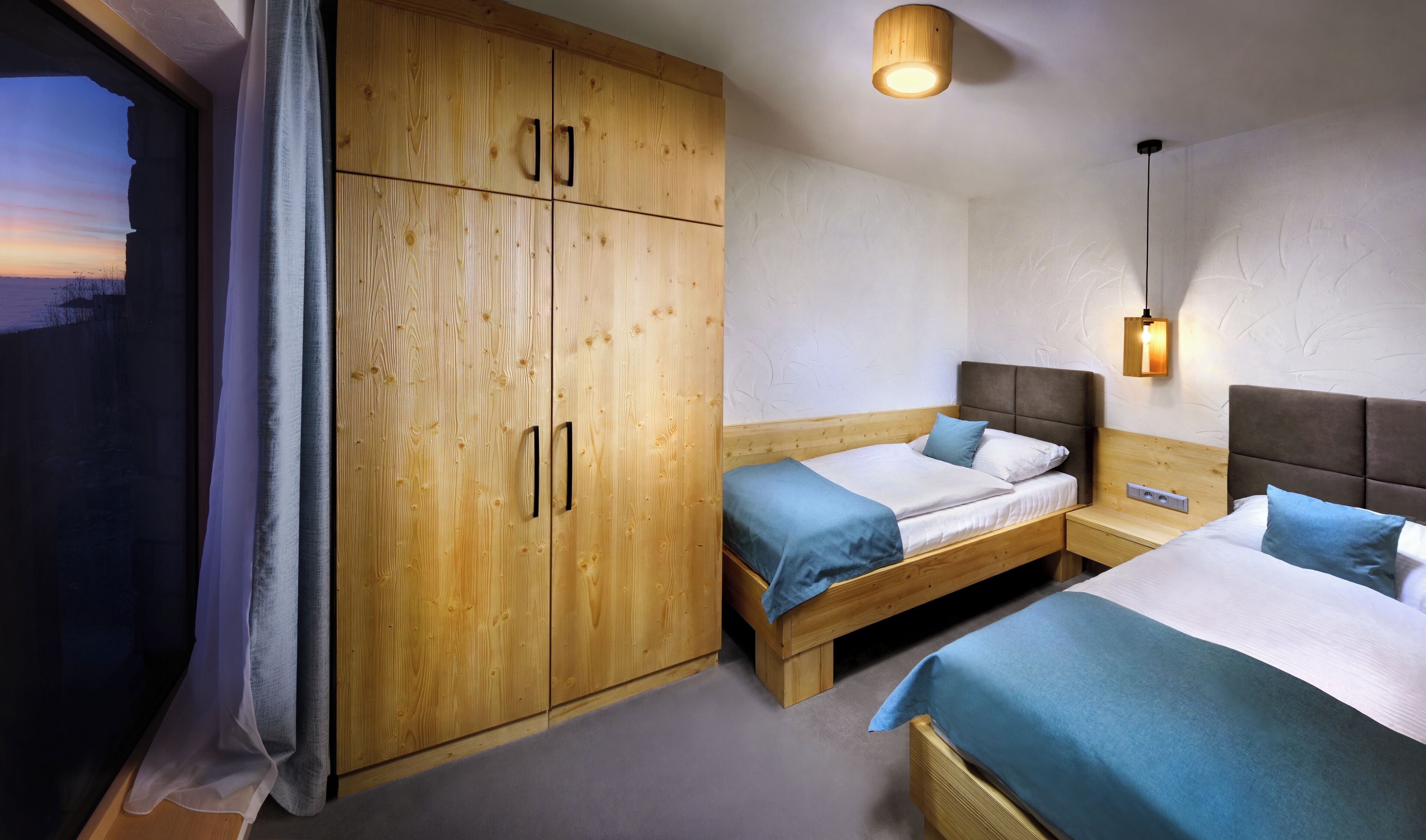 Ein Hotelzimmer mit zwei Betten, einem Holzschrank, einem Fenster mit Vorhängen und einer Wandleuchte.