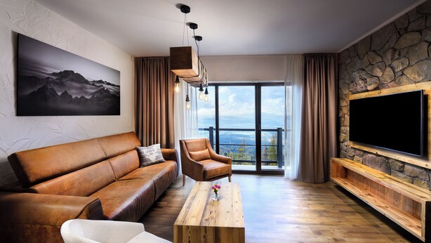 A modern living room with a leather sofa, a wooden coffee table, and a large TV mounted on a stone wall. - APLEND Monte Móry (Štrba)