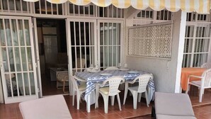 Un'area patio con un tavolo apparecchiato per mangiare, due poltrone relax e una zona salotto coperta.