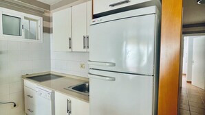 Una cucina compatta con mobili bianchi, lavastoviglie integrata e frigorifero.