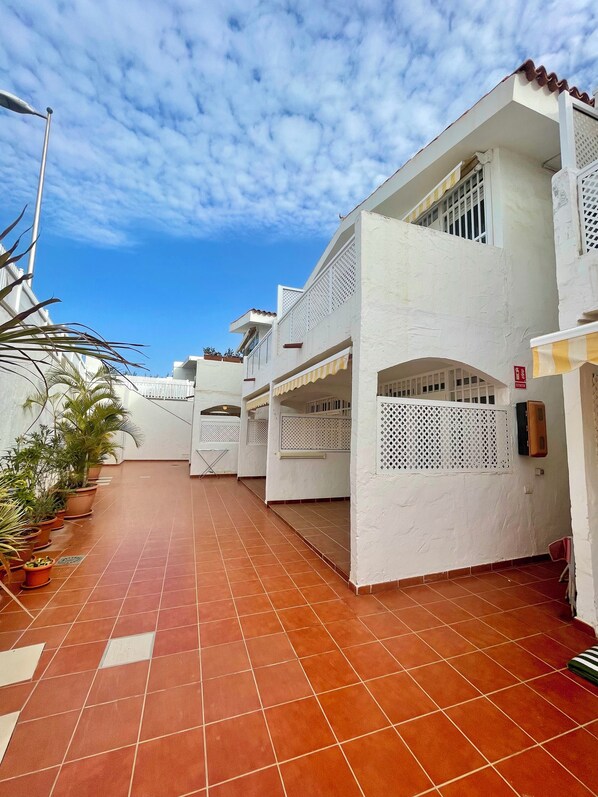 A corridor with white buildings, potted plants, and a tiled floor.