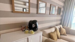 Camera d'albergo con parete a righe, un divano bianco, un mobiletto bianco e una macchina per il caffè sul ripiano.