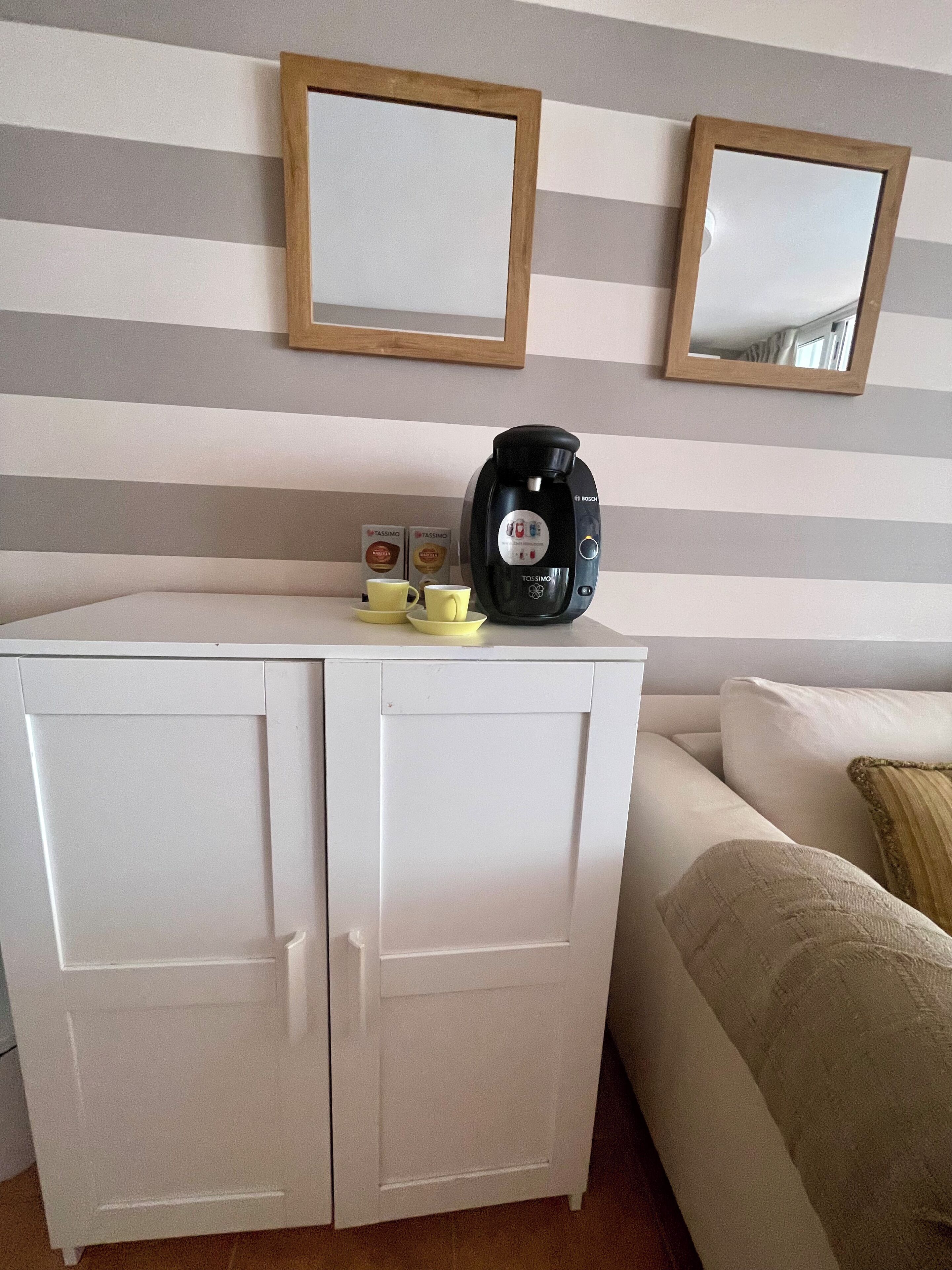 A kitchenette with a coffee maker, two cups, and a box of Tassimo pods.