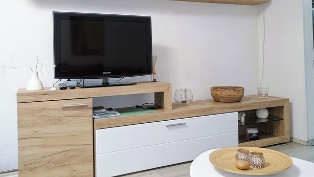 A modern living room with a flat-screen TV, wooden cabinets, a white table, and a decorative bowl. - Vacation apartment for 2 near Spreewald & Schlaubetal - quiet location  (Lieberose)