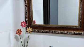 Un baño con lavamanos de mármol, un espejo con marco decorativo y un florero con flores.
