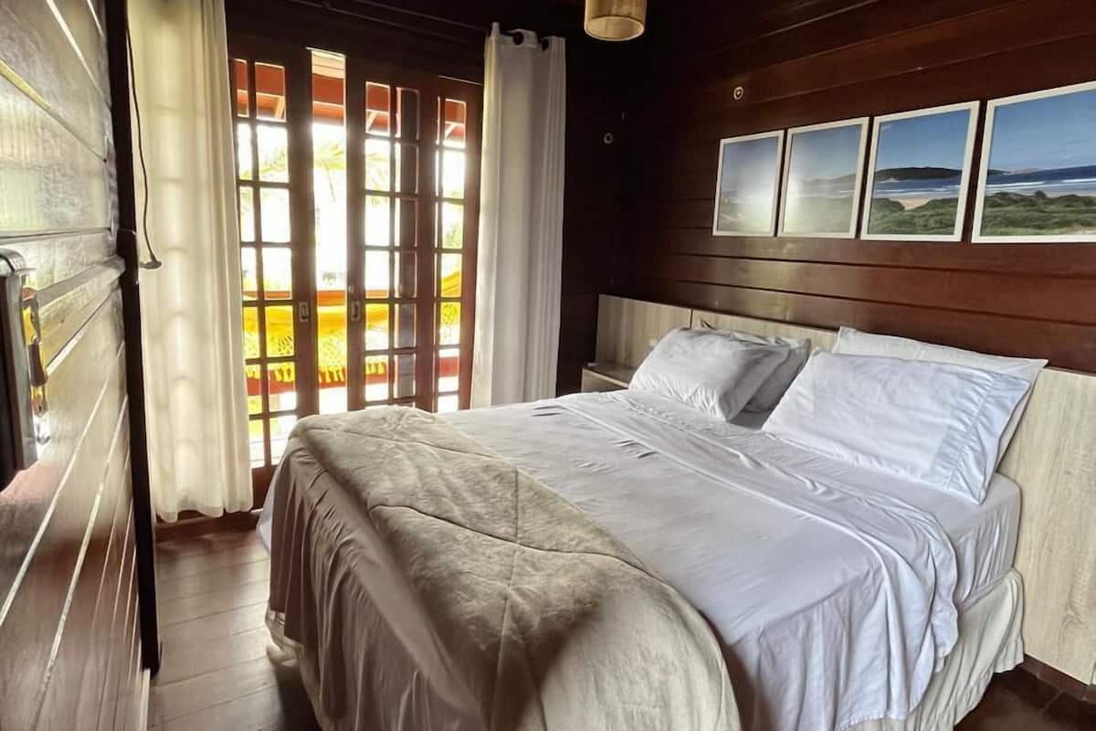 A bedroom with a wooden ceiling, a bed with white bedding, and a window with curtains.
