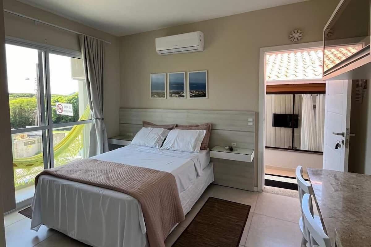 A bedroom with a bed, bedside tables, a TV, and a view of the outdoors.