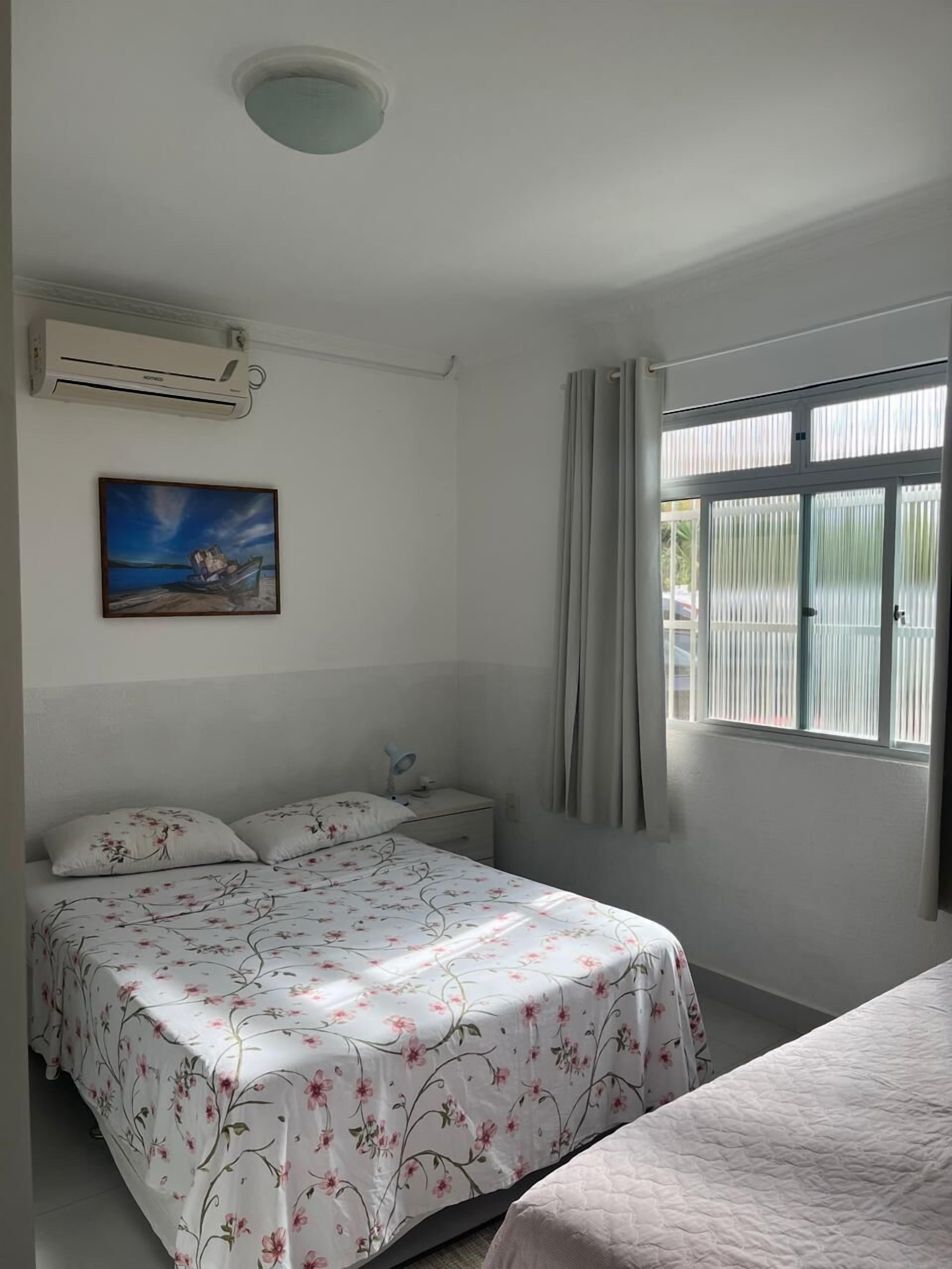 A bedroom with a bed, a nightstand, a painting, and a window with curtains.