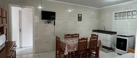 A compact kitchen with a dining area, a TV mounted on the wall, and a small refrigerator.