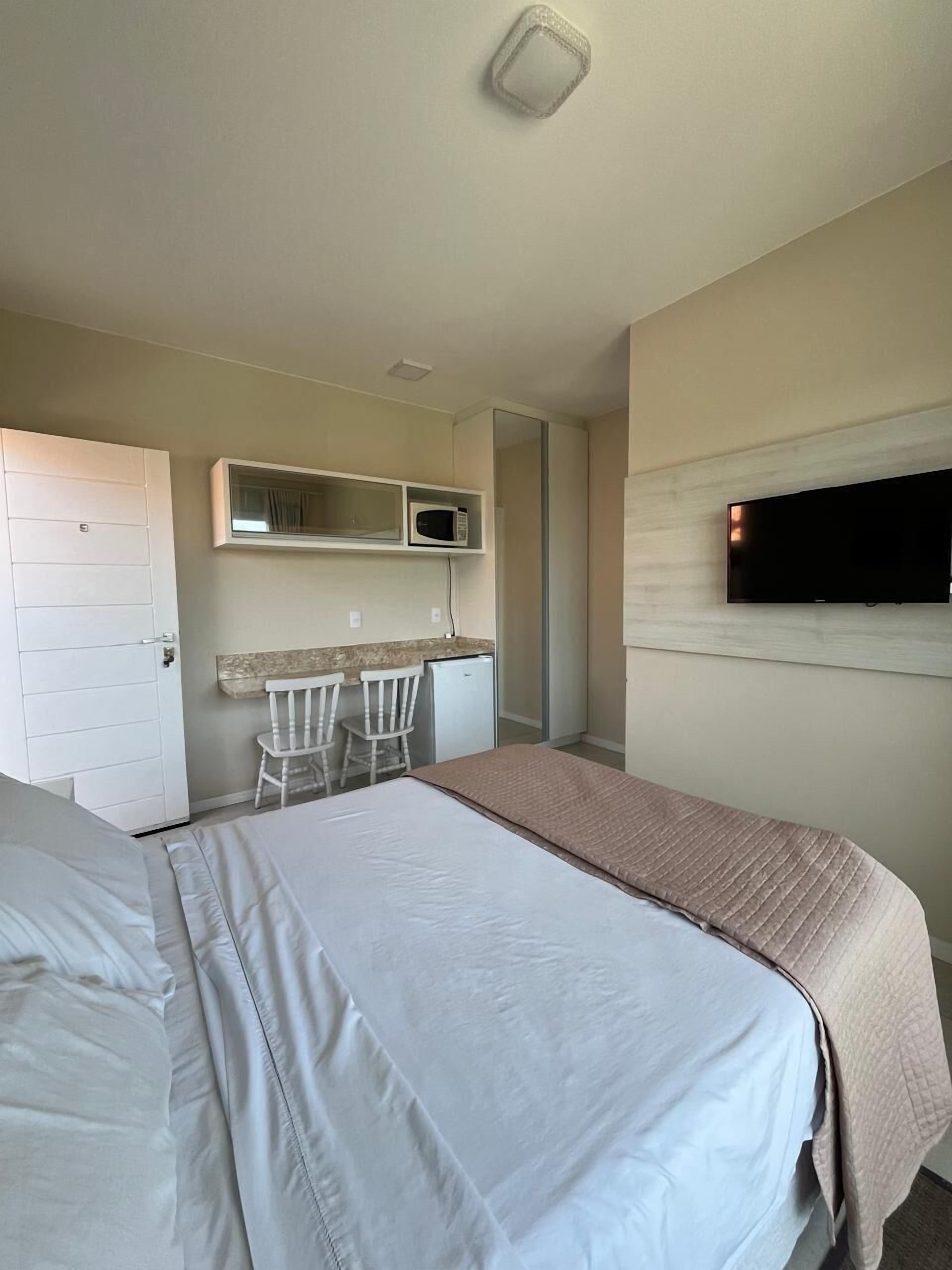 A bedroom with a bed, a desk with a chair, a microwave, and a TV.