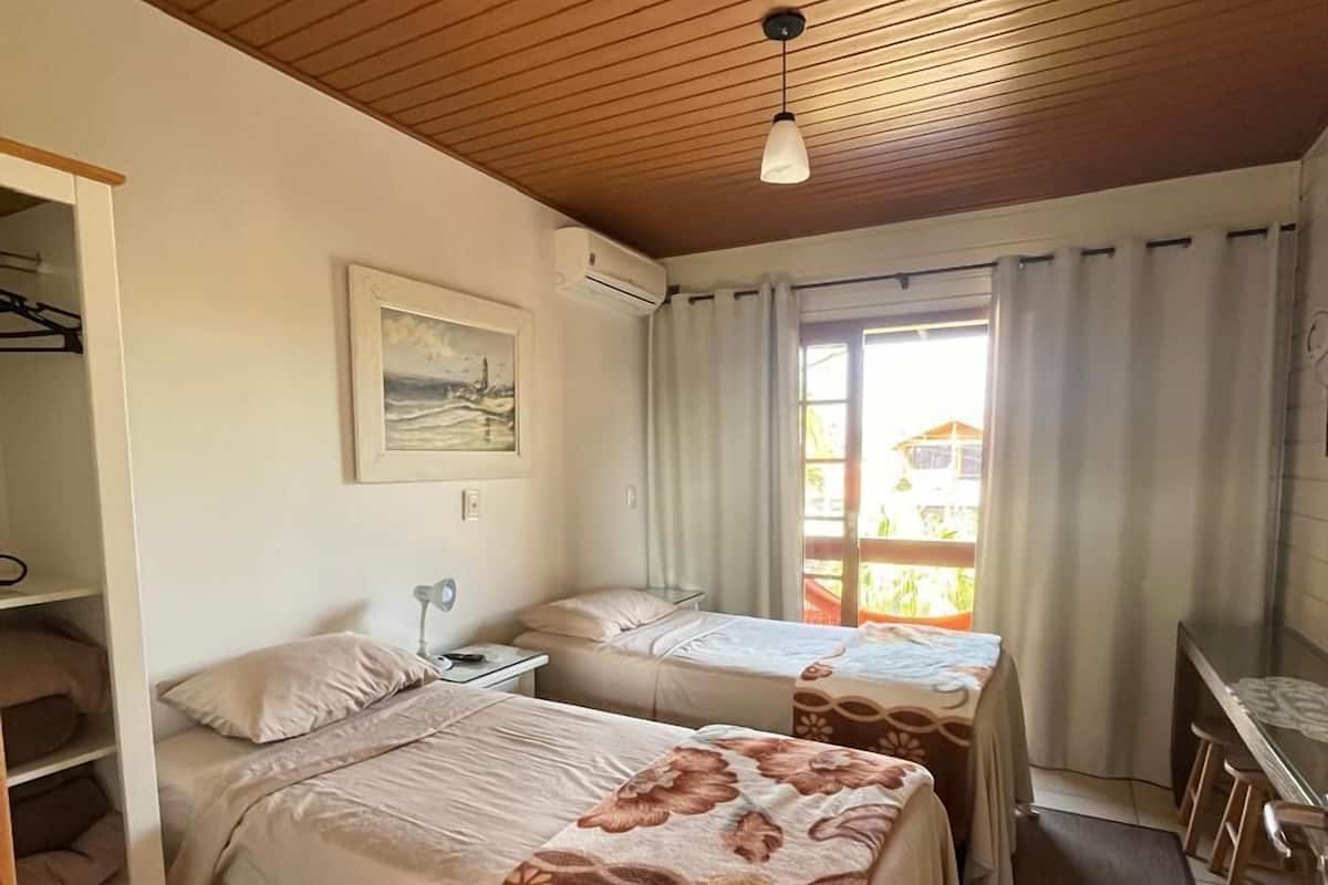 A bedroom with two beds, a desk, a chair, and a window with curtains.