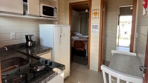 A compact kitchen with a gas stove, microwave, and coffee maker. A small sink is visible, and a white chair is placed near the kitchen counter. - Pousada Recanto do Neca (Florianópolis)
