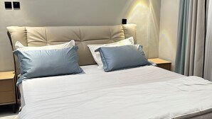 A modern bedroom with a large bed, two nightstands, and a wall-mounted light fixture. - Nsiimenta Stay (Kampala)