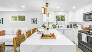 A modern kitchen with white cabinetry, a marble island, and a dining area with wooden chairs.