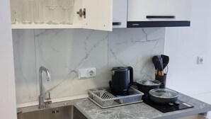 Eine moderne Küche mit weißen Schränken, einer Marmorarbeitsplatte, einer Edelstahlspüle und einer Kaffeemaschine.