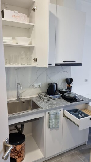 Een koelkast, een kookplaat, een waterkoker, kookgerei, borden en bestek