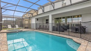 A swimming pool with a glass enclosure, lounge chairs, and a covered patio area.