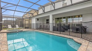 A swimming pool with a glass enclosure, lounge chairs, and a covered patio area.