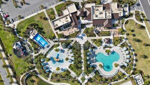 An aerial view of a resort with multiple swimming pools, a children's play area, and a variety of outdoor seating areas.
