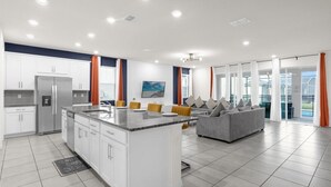 Una cocina moderna con armarios blancos, una isla central y un sofá gris en la zona de estar.